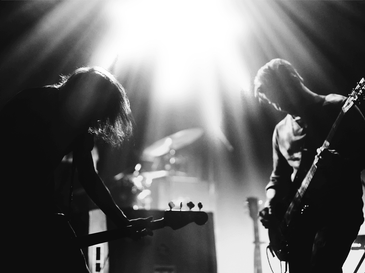 High-contrast black-and-white photograph of two musicians silhouetted on stage under a bright spotlight